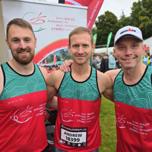 Three smiling men wearing Wales Air Ambulance running vests, about to start a half marathon