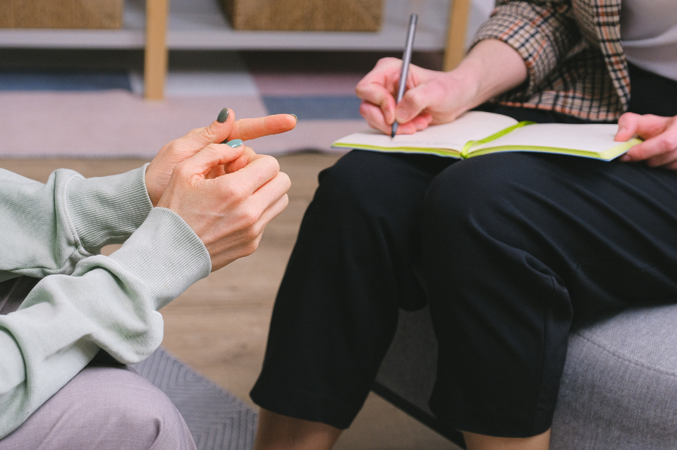 Image of two people chatting showing only their legs and a clipboard taking notes
